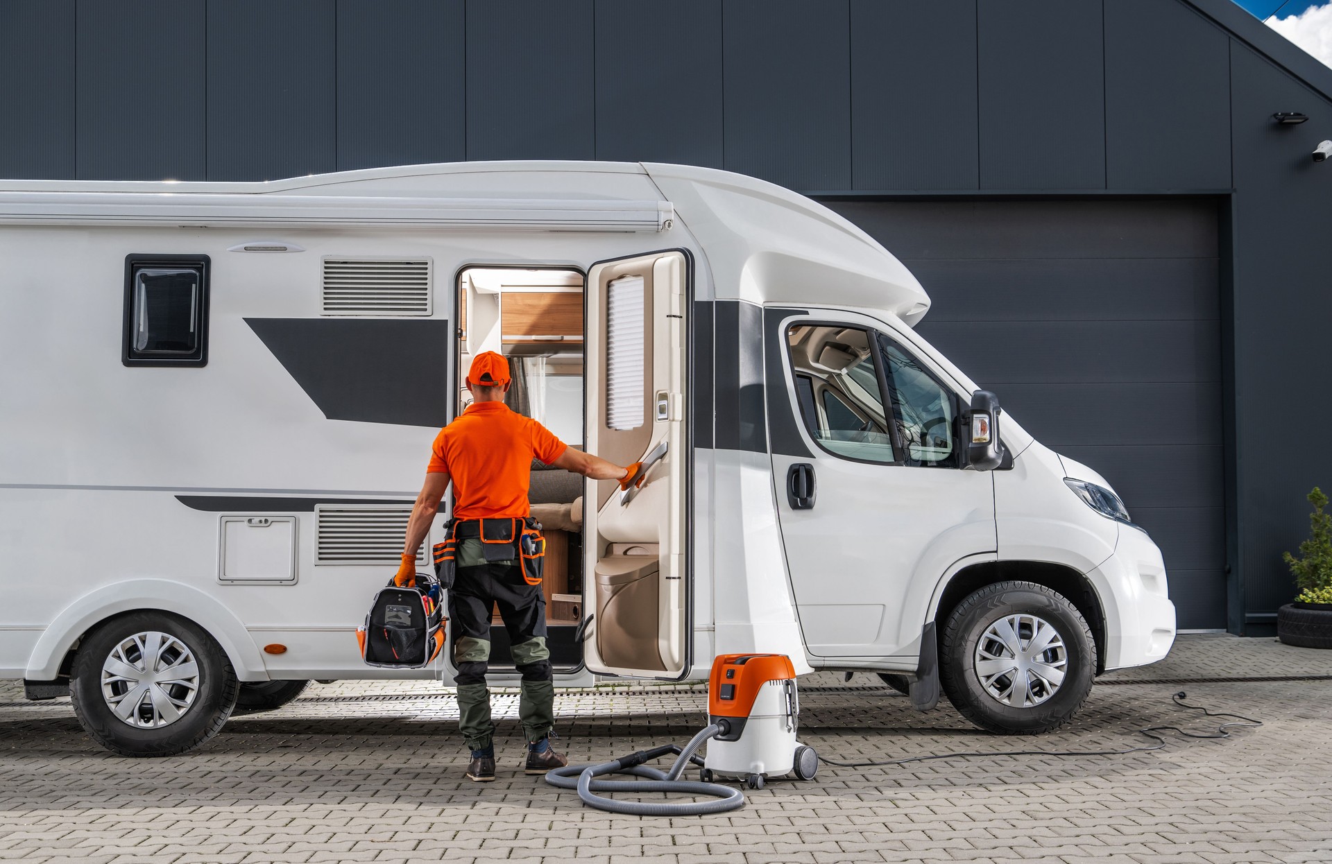 Technician Cleaning a White Motorhome With a Vacuum and Repairing RV Appliances