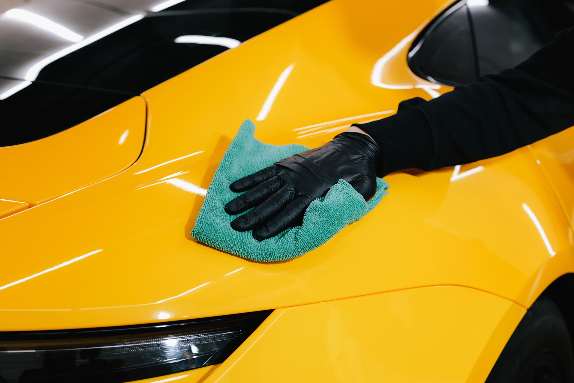 Manual washing and polishing car with microfiber cloth after detailing procedure. Microfiber hand cleaning and washing sports car using microfiber towel in garage.